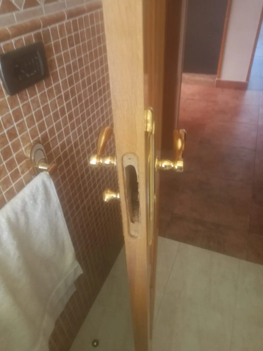 Puerta de baño con manilla dorada y cerradura de condena, vista desde dentro del aseo