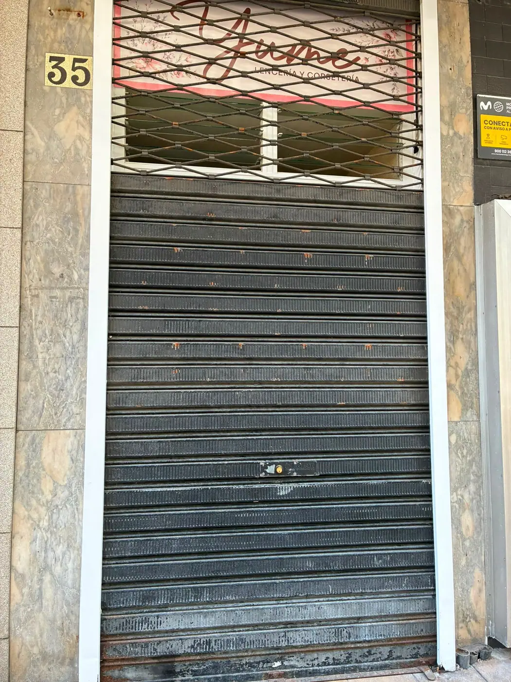 Persiana metálica enrollable de un local a pie de calle, subida a media altura