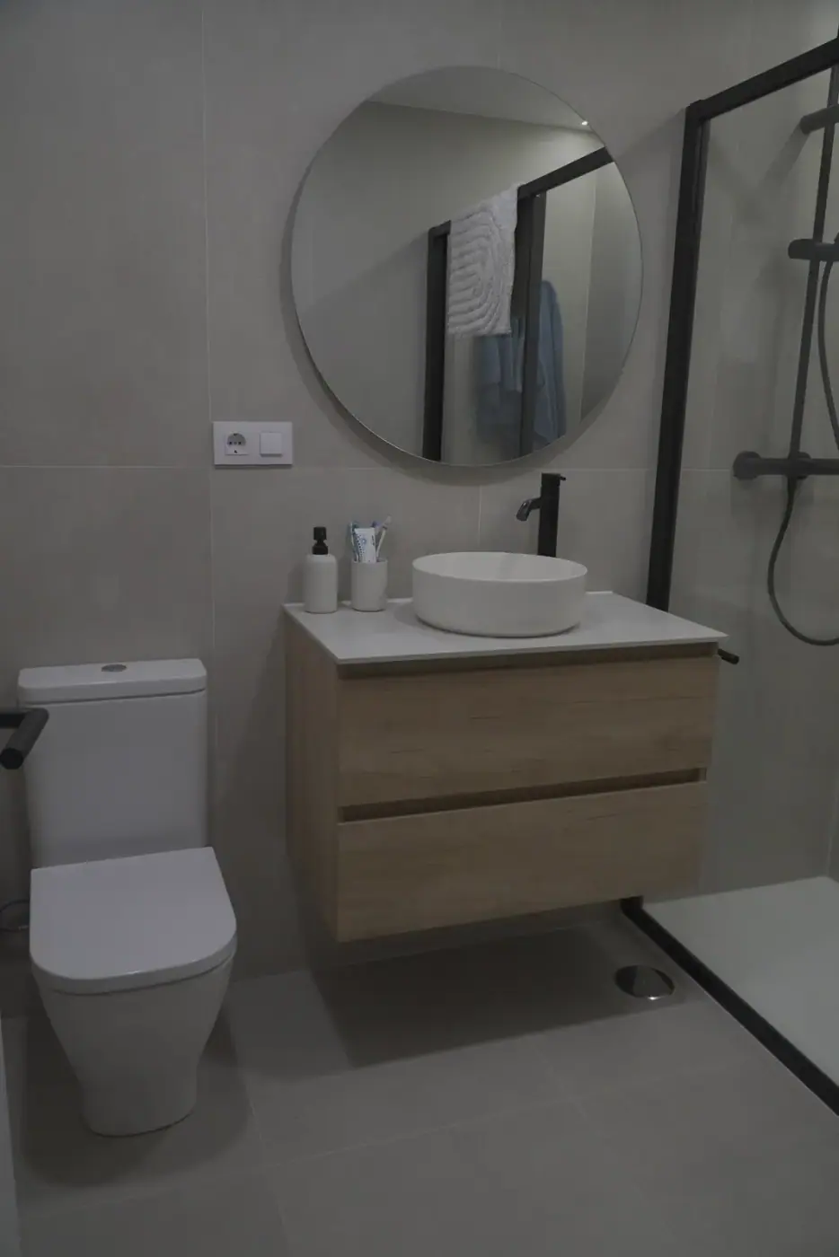 Lavabo de sobre encimera con mueble de madera y espejo redondo en baño reformado