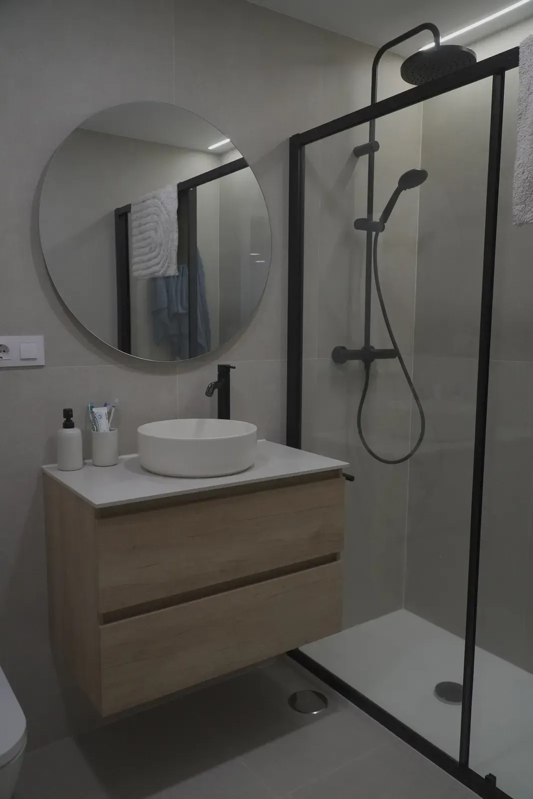 Baño reformado con ducha de perfil negro, mueble de madera y lavabo sobre encimera