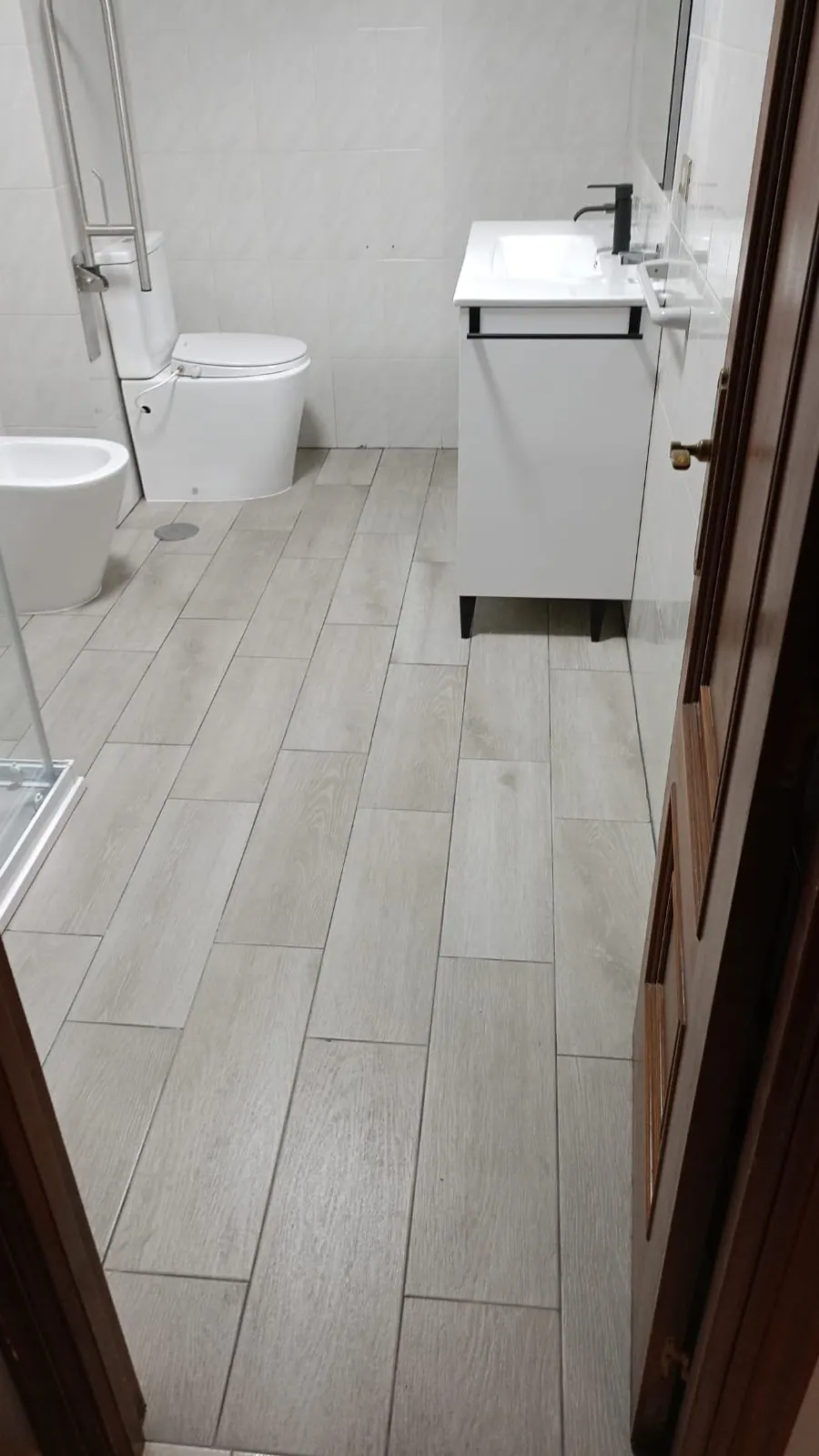 Baño terminado en A Coruña con suelo porcelánico imitación madera, mueble suspendido blanco y grifería negra