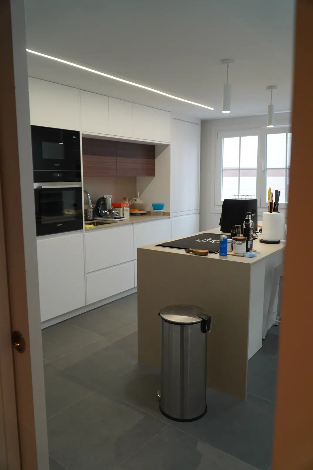 Cocina reformada blanca con detalles de madera e iluminación lineal