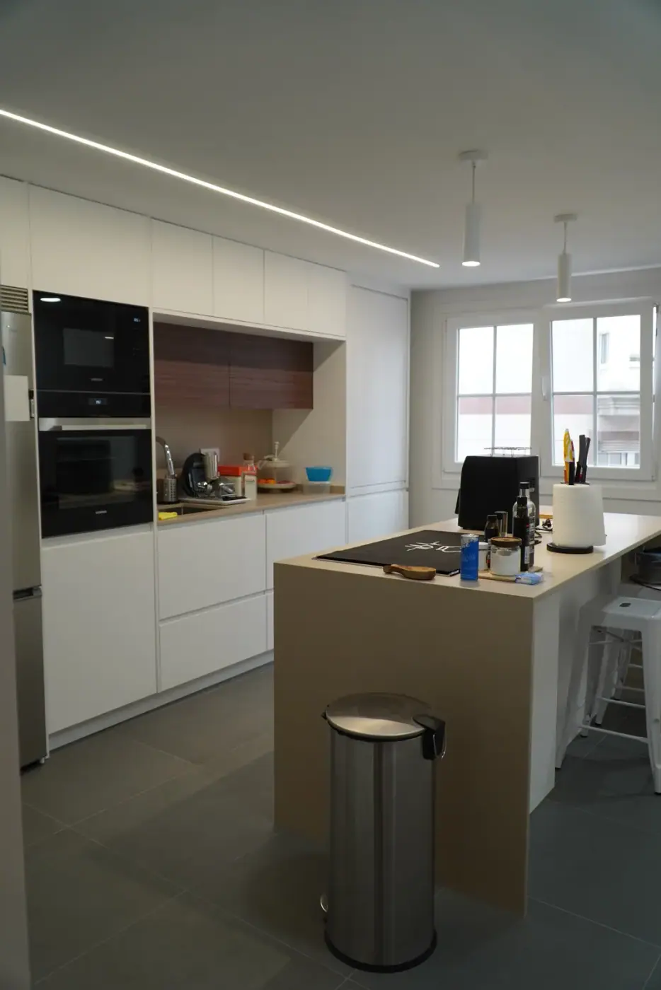 Cocina blanca reformada con isla central, columna de horno y microondas