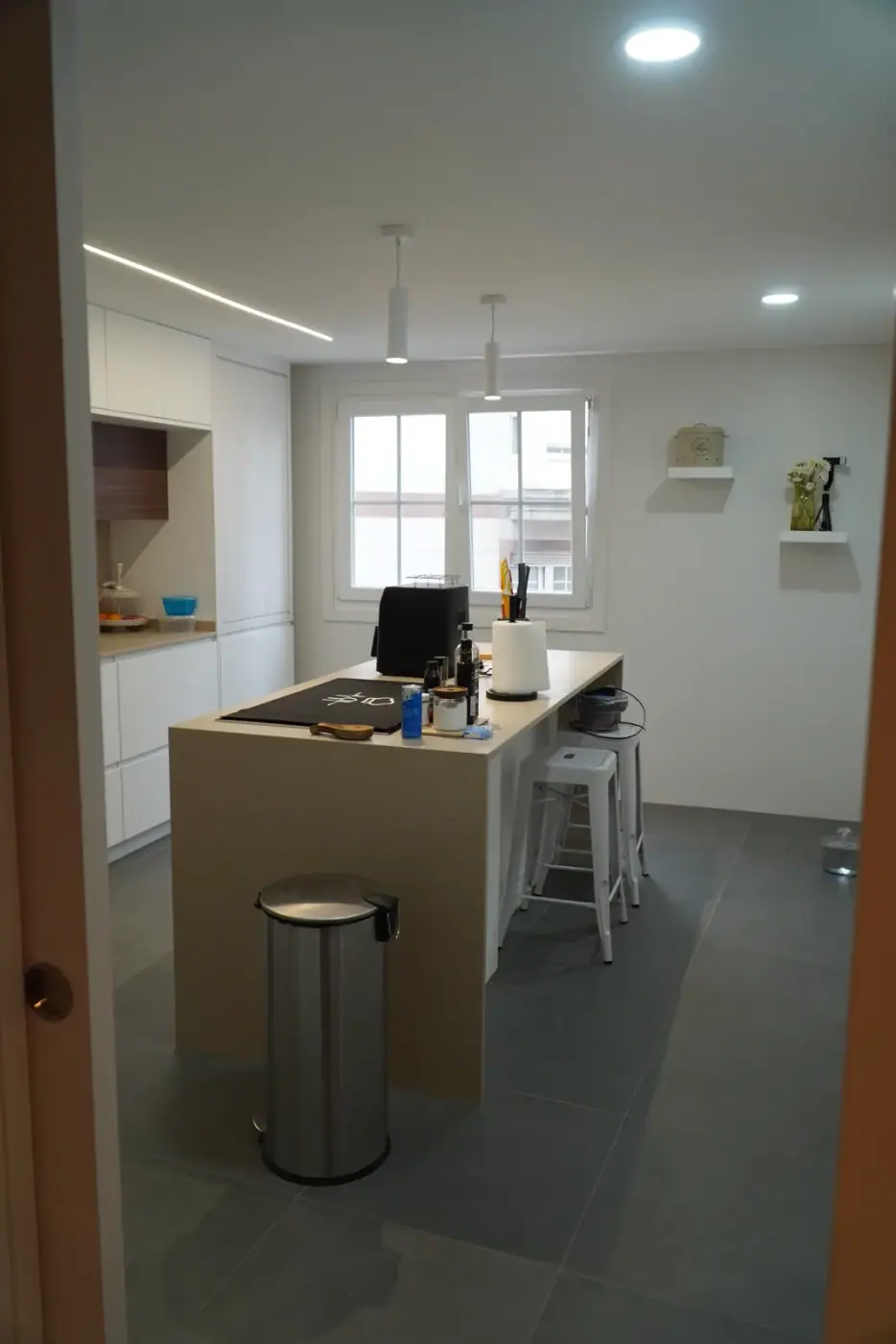 Isla de cocina con encimera de madera y taburetes, con la galería al fondo